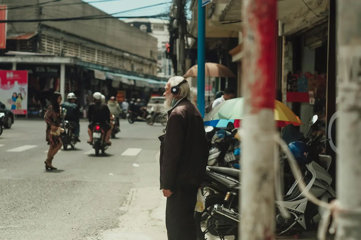 Elderly man standing at the edge of a busy street, paused between moments in an everyday urban scene. Used to illustrate the concept of missed moments in photography