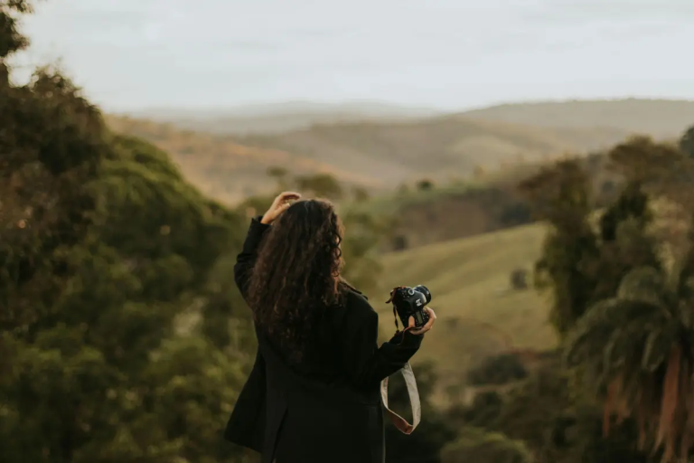 Photographer standing in a natural landscape holding a camera without actively shooting. Used to illustrate the concept of working without a shot list.